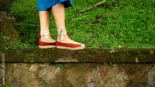 Legs of a European girl in a blue dress walking in shoes on green grass