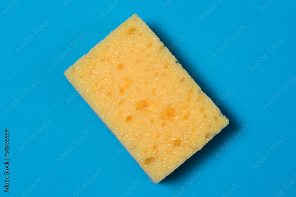Yellow porous sponge for cleaning and washing dishes on a blue background with copy space. Homework concept.
