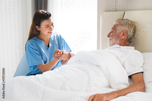 Happy Asian nurse or caregiver holding elderly man patient hand on the bed with care