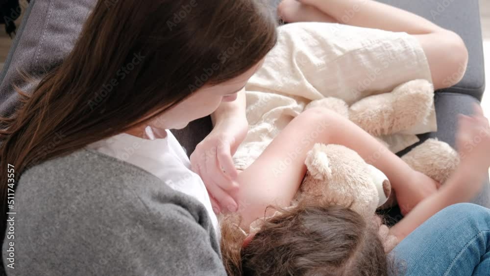 Loving mom embrace kid daughter cuddling enjoy time together at home, caring young mother sitting on sofa hugging cute little girl rest on comfortable couch, mommy and child relax feel love connection Loving mom embrace kid daughter cuddling enjoy time together at home, caring young mother sitting on sofa hugging cute little girl rest on comfortable couch, mommy and child relax feel love connection