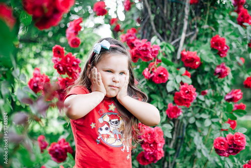 close-up portrait of a frowning, anxious girl in a red T-shirt holding her cheeks under the arch of a wild rose.