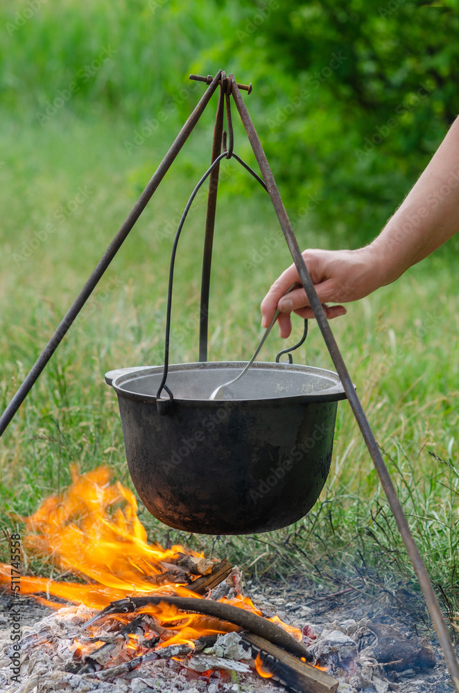 a pot in which soup is cooked on a tripod stands on a fire a pot in which soup is cooked on a tripod stands on a fire