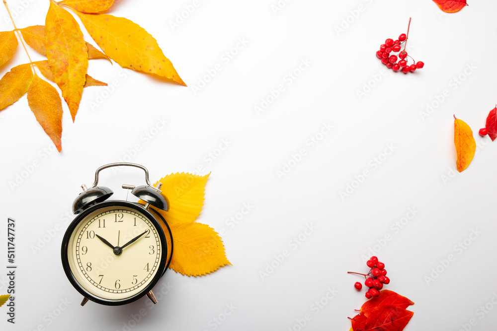Yellow autumn leaves and an alarm clock on a white background, a thematic layout about the autumn mood
