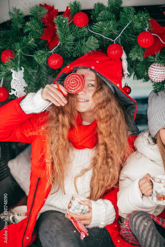 Young smiling teenage girl in coat and red hat hiding behind lollipop. Outdoor party in car trunk, winter holiday for redhaired teen girl, photo