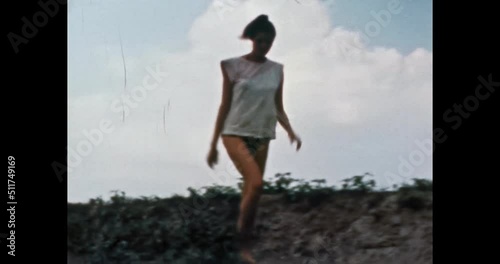 Beautiful model woman in swimsuit in sunny summer, on blue sky, green nature. Girl long, thin legs in Bikini goes in vintage color film. Rest, vacation at weekend. Family archive. Retro 1980s. 4K