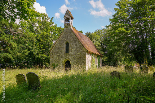 Small rural church in English countryside. Quaint village church viewed from overgrown churchyard. Pretty stone church hidden among the trees 