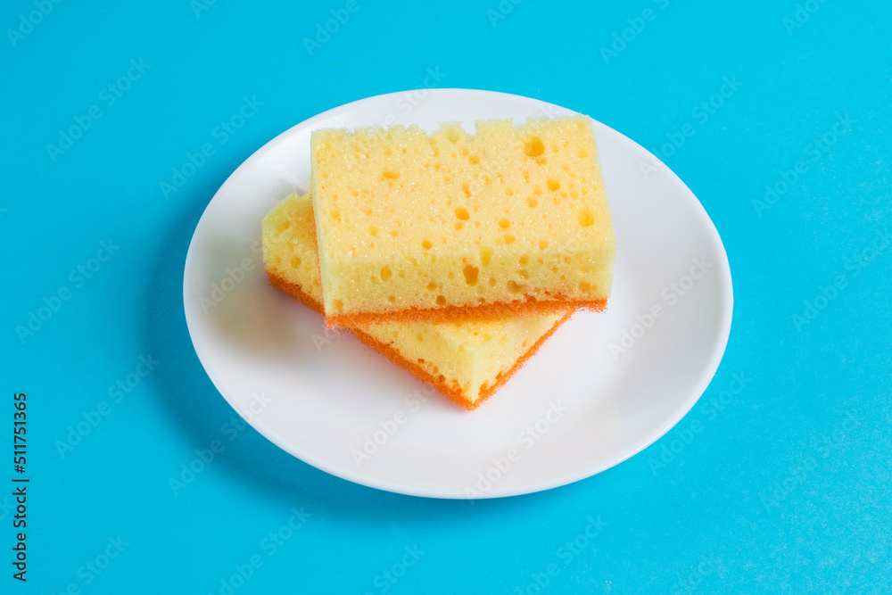 Sponges for washing dishes and cleaning in the apartment on a plate on a blue background. The concept of using ecological detergents for the home