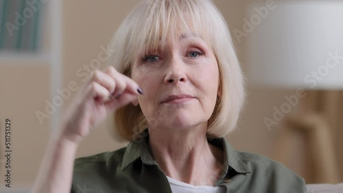 Close-up portrait old caucasian 60s woman elderly lady grandmother zipping lips locking mouth imitates throwing away key keep secret mystery silence gesture secrecy information stop talking gesture