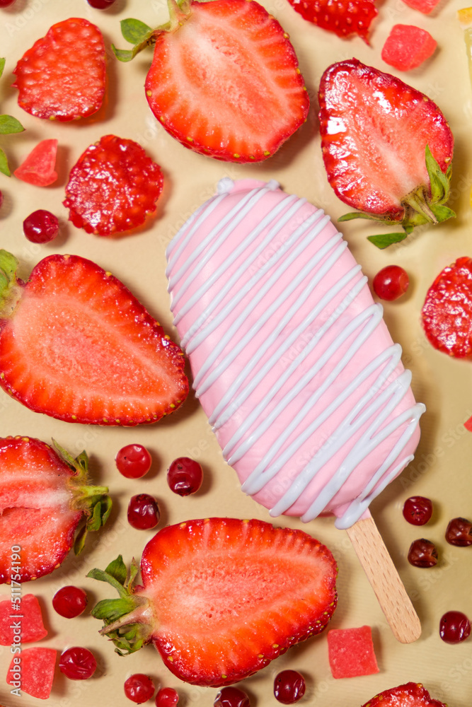 Pink ice cream on a stick with strawberries and red lingonberries on a beige background.