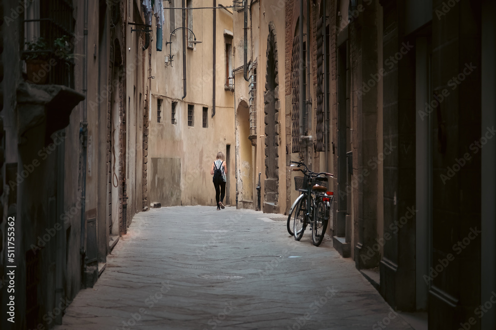 Woman walks alone in alley way in the medieval city of Lucca, Italy.