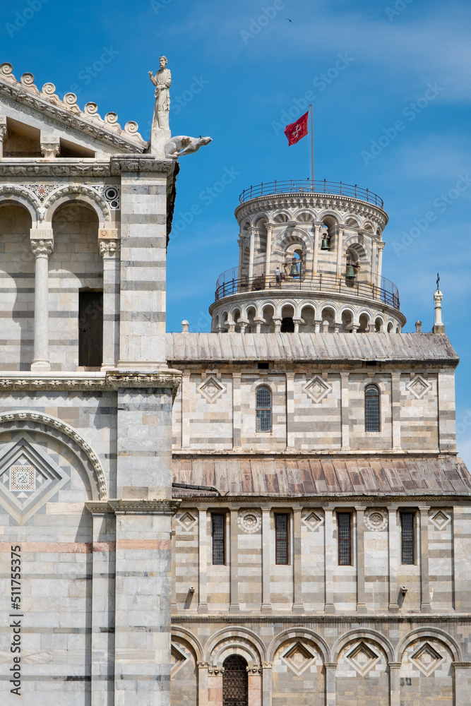 Naklejka premium Leaning tower of Pisa peaking from behind Pisa Cathedral with brilliant blue sky.