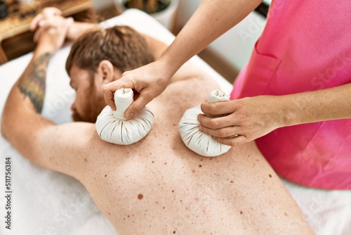 Young redhead man having back massage using thai bags at beauty center