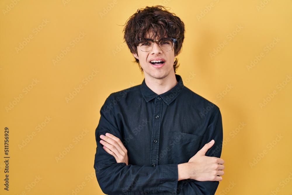 Obraz premium Young man wearing glasses over yellow background skeptic and nervous, disapproving expression on face with crossed arms. negative person.