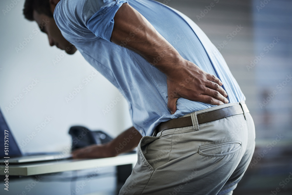 Its so painful I cant even stand up properly. Shot of a young businessman suffering with back pain at work. - obrazy, fototapety, plakaty 