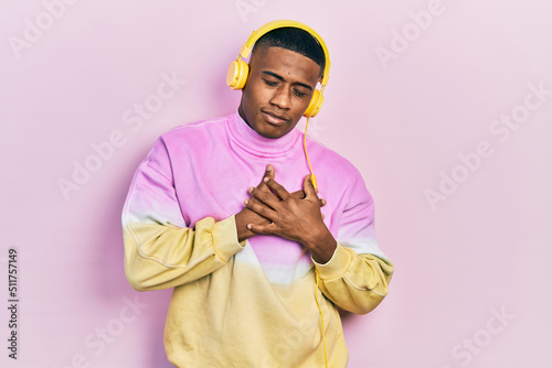 Young black man listening to music wearing headphones smiling with hands on chest with closed eyes and grateful gesture on face. health concept.