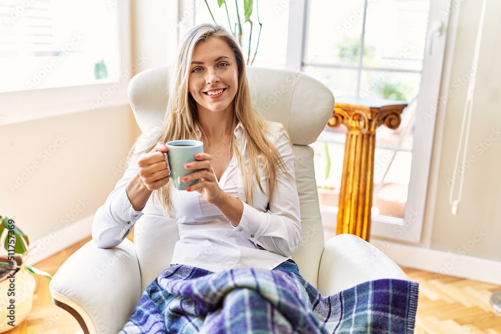 Young blonde woman drinking cup of coffee sitting on armchair at home. Young blonde woman drinking cup of coffee sitting on armchair at home.