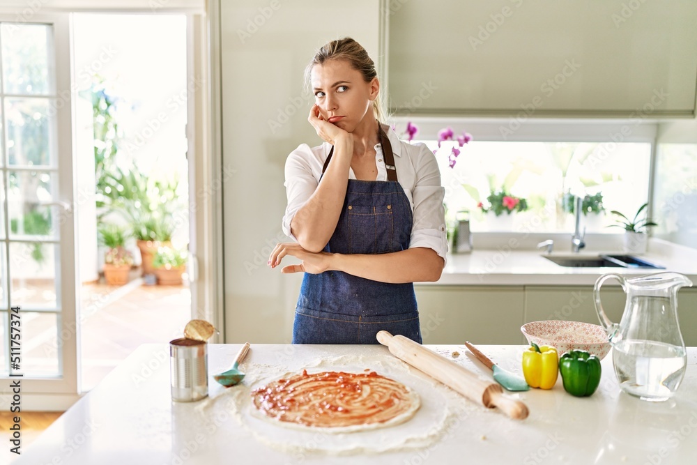 Beautiful blonde woman wearing apron cooking pizza thinking looking tired and bored with depression problems with crossed arms.