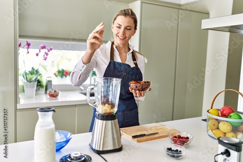 Young blonde woman smiling confident pouring dates on blender at kitchen