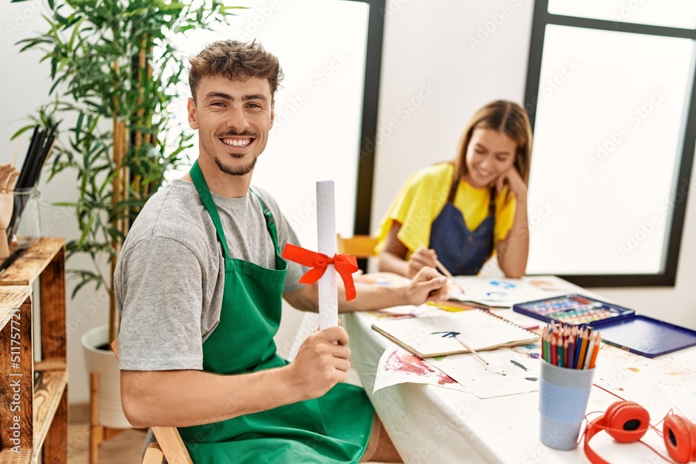 Young hispanic artist couple smiling happy drawing at art studio. Man holding diploma sitting on the table. Young hispanic artist couple smiling happy drawing at art studio. Man holding diploma sitting on the table.