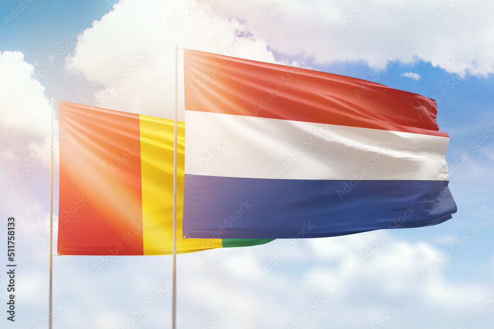 Sunny blue sky and flags of netherlands and guinea Sunny blue sky and flags of netherlands and guinea