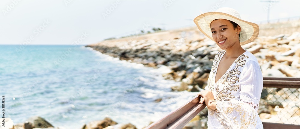 Young hispanic woman smiling confident wearing summer hat at seaside