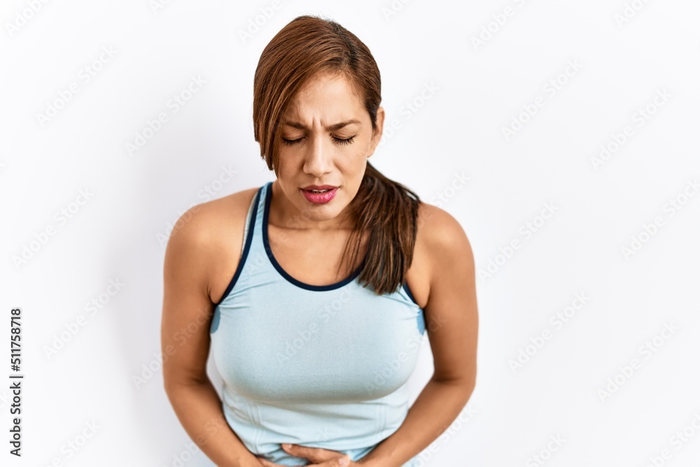 Young latin woman wearing sporty clothes over isolated background with hand on stomach because indigestion, painful illness feeling unwell. ache concept. Young latin woman wearing sporty clothes over isolated background with hand on stomach because indigestion, painful illness feeling unwell. ache concept.