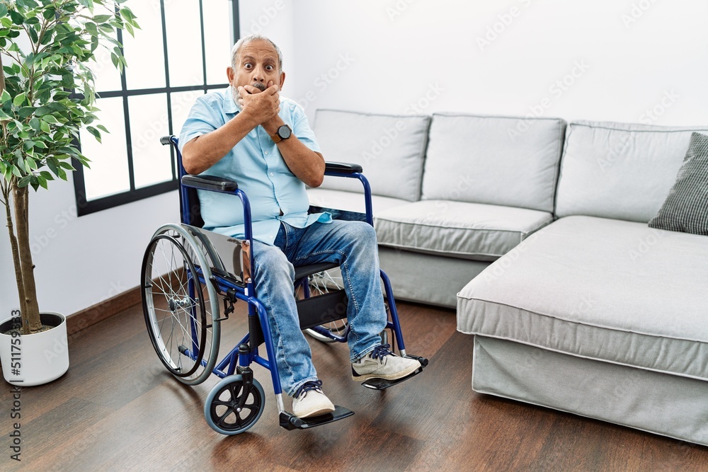 Handsome senior man sitting on wheelchair at the living room shocked covering mouth with hands for mistake. secret concept. Handsome senior man sitting on wheelchair at the living room shocked covering mouth with hands for mistake. secret concept.