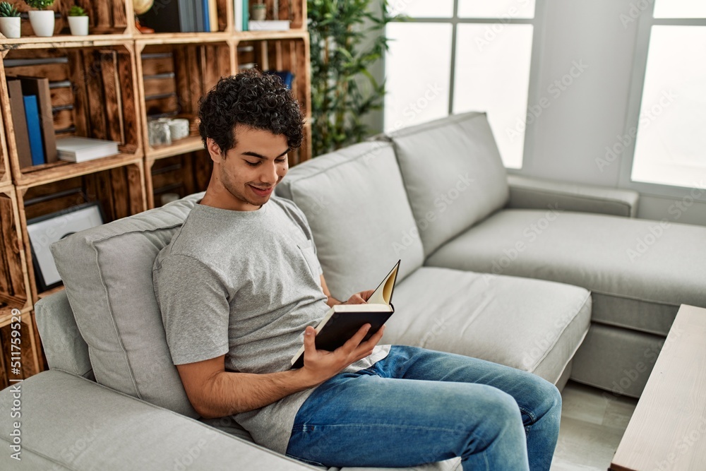 Young hispanic man reading book sitting on the sofa at home. Young hispanic man reading book sitting on the sofa at home.