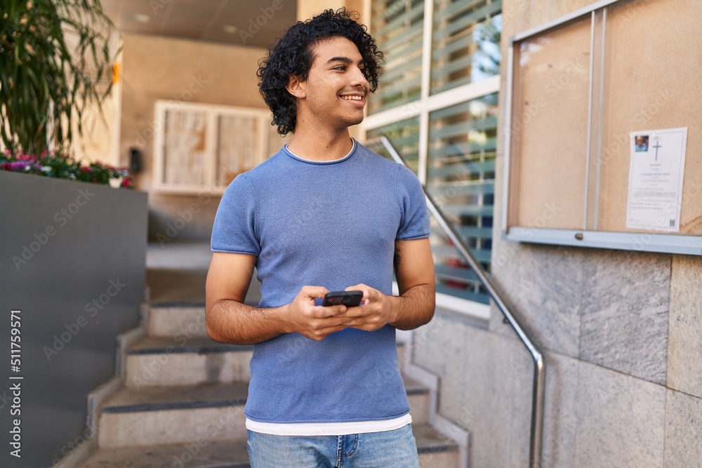 Fototapeta premium Young hispanic man smiling confident using smartphone at street