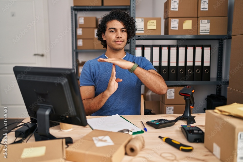 Fototapeta premium Hispanic man with curly hair working at small business ecommerce doing time out gesture with hands, frustrated and serious face