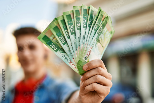 Young caucasian guy smiling holding russian ruble banknotes at the city photo