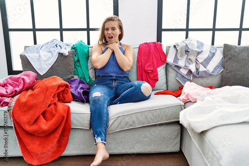 Young caucasian woman sitting on the sofa at home around dirty laundry shouting and suffocate because painful strangle. health problem. asphyxiate and suicide concept. © Krakenimages.com