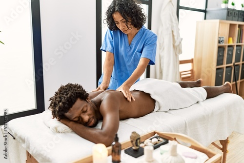 Young physiotherapist woman giving back massage to african american man at the clinic.