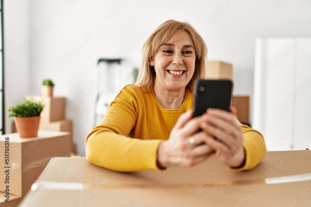 Middle age blonde woman smiling happy using smartphone at new home. Middle age blonde woman smiling happy using smartphone at new home.