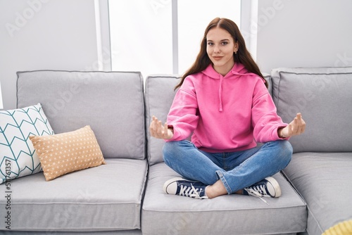 Young woman doing yoga exercise sitting on sofa at home