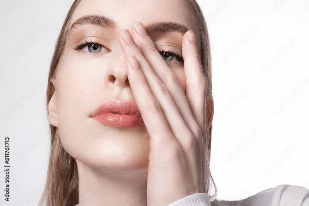 Close up woman with beautiful blue eyes and perfect clear skin with natural makeup looks at the camera covering half of her face with her hand. Close up woman with beautiful blue eyes and perfect clear skin with natural makeup looks at the camera covering half of her face with her hand.