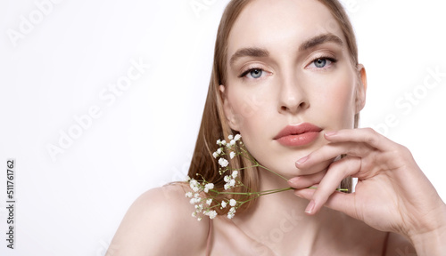 A blonde-haired girl with a perfect clean face and natural makeup with white flowers in her hand. Beautiful cosmetic portrait