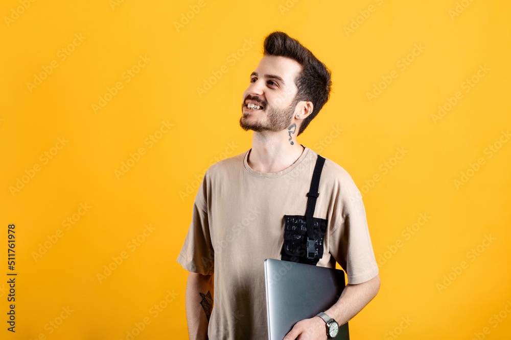 Caucasian young man wearing t-shirt posing isolated over yellow background holding in hands carrying laptop posing. Looking at the camera with big smiles. Caucasian young man wearing t-shirt posing isolated over yellow background holding in hands carrying laptop posing. Looking at the camera with big smiles.