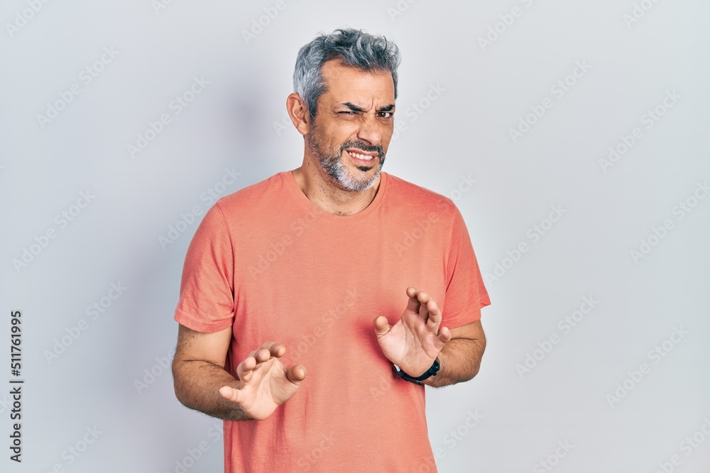 Handsome middle age man with grey hair wearing casual t shirt disgusted expression, displeased and fearful doing disgust face because aversion reaction. with hands raised
