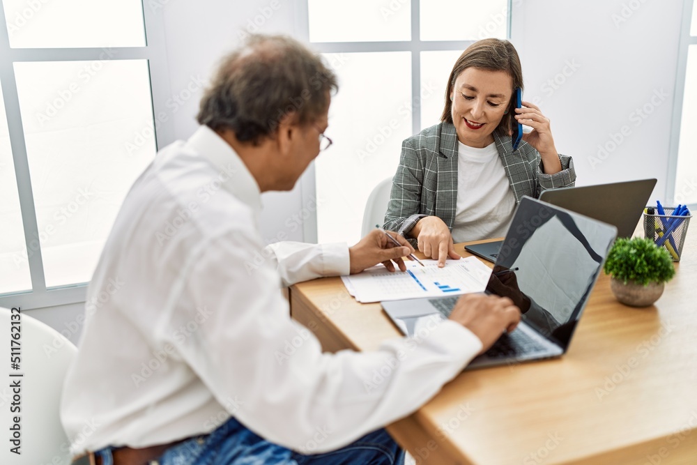 Middle age man and woman business workers using laptop and talking on the smartphone at office Middle age man and woman business workers using laptop and talking on the smartphone at office