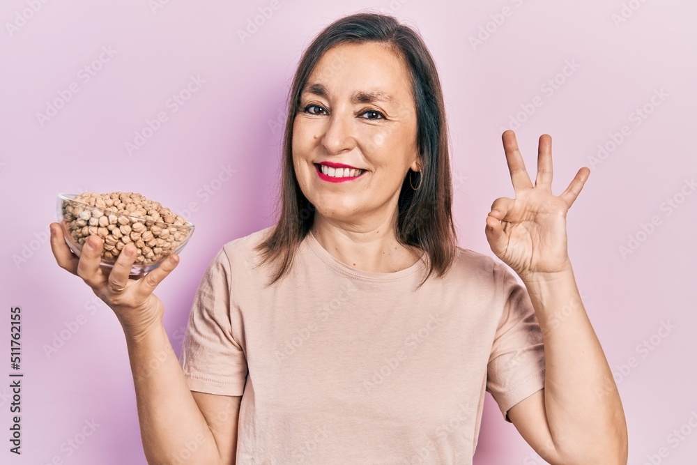 Middle age hispanic woman holding chickpeas bowl doing ok sign with fingers, smiling friendly gesturing excellent symbol Middle age hispanic woman holding chickpeas bowl doing ok sign with fingers, smiling friendly gesturing excellent symbol