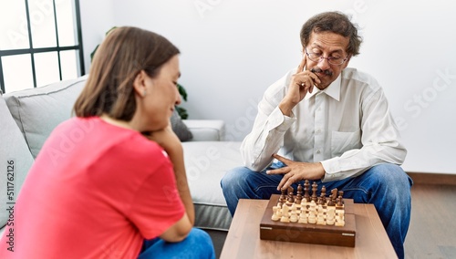 Middle age man and woman couple concentrate playing chess at home