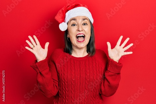 Middle age hispanic woman wearing christmas hat celebrating crazy and amazed for success with arms raised and open eyes screaming excited. winner concept © Krakenimages.com