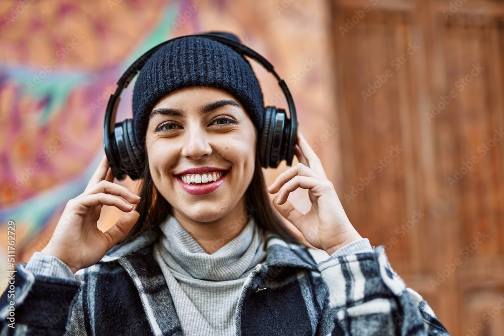 Young hispanic woman smiling happy using headphones at the city.