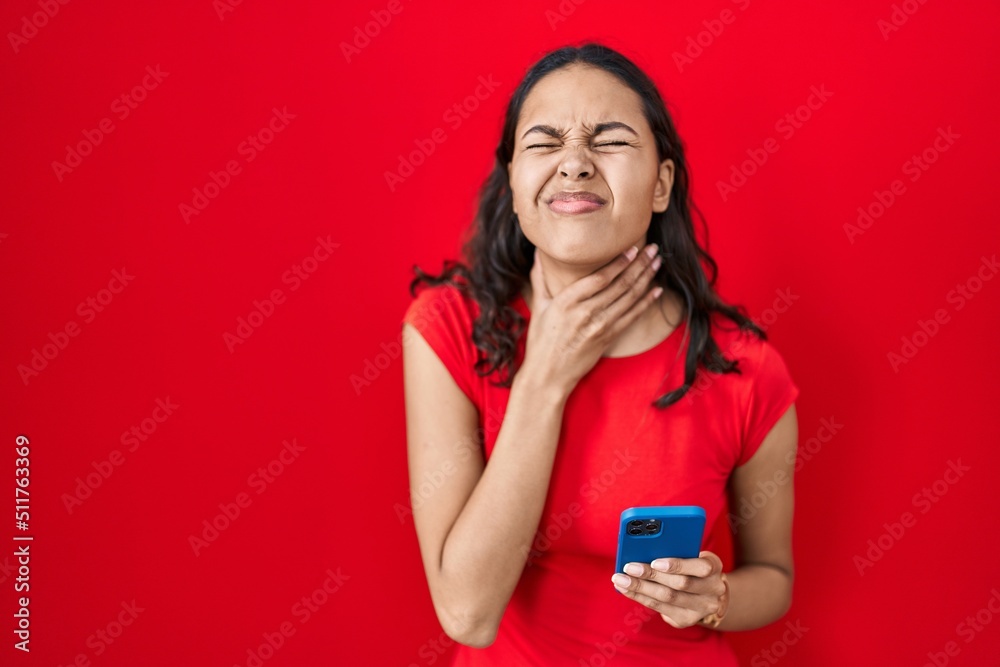 Young brazilian woman using smartphone over red background touching painful neck, sore throat for flu, clod and infection Young brazilian woman using smartphone over red background touching painful neck, sore throat for flu, clod and infection