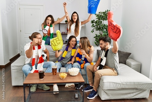 Group of young friends watching and supporting soccer match at home.