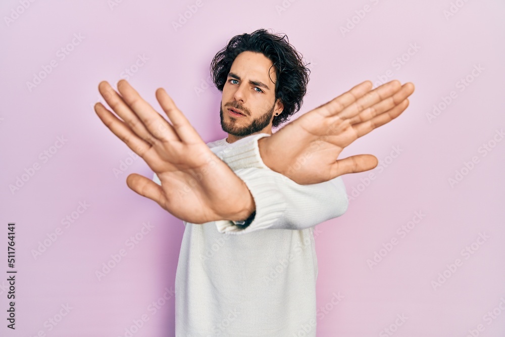 Handsome hispanic man wearing casual white sweater rejection expression crossing arms and palms doing negative sign, angry face Handsome hispanic man wearing casual white sweater rejection expression crossing arms and palms doing negative sign, angry face