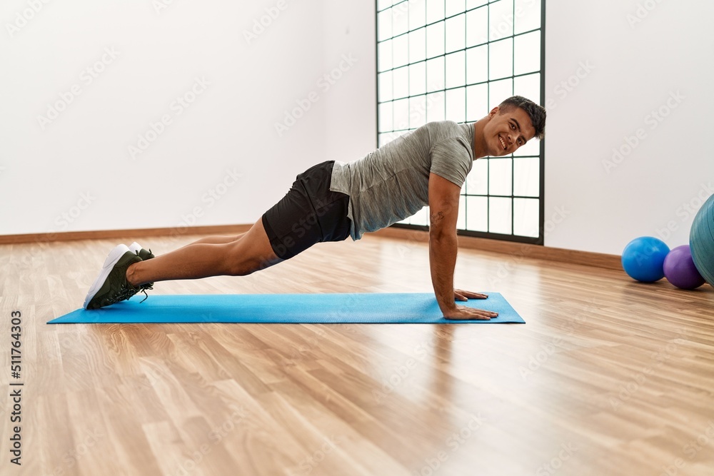 Young hispanic man smiling confident stretching at sport center