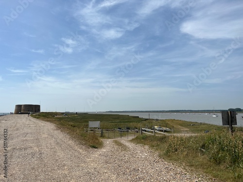  Landscape with Martello tower historic stone forts built as 19th century sea defences on East Anglia coastline Aldeburgh beach Suffolk uk with wooden bridge over moat in Summer blue skies 