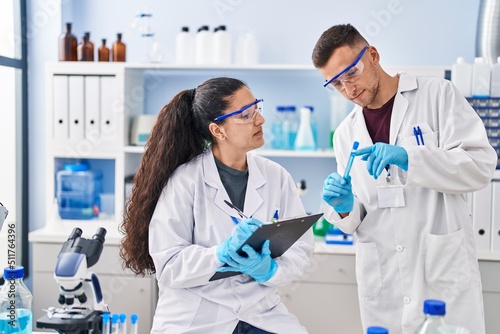 Man and woman wearing scientist uniform write on clipboard holding test tube at laboratory